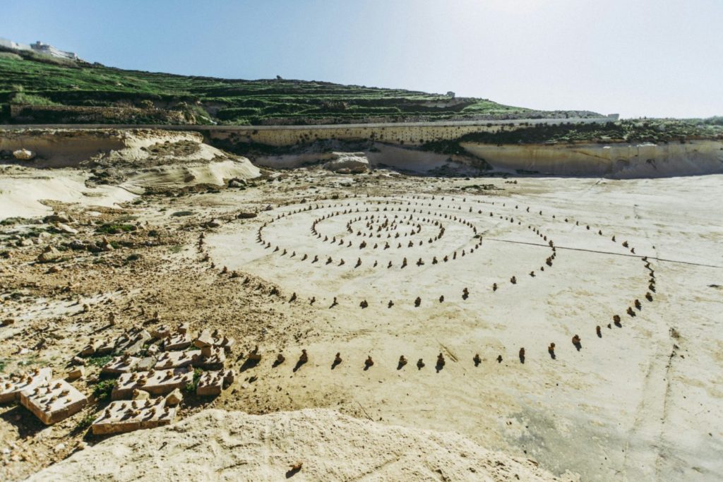 spiral of rocks on sand with mountains and greenery in the background